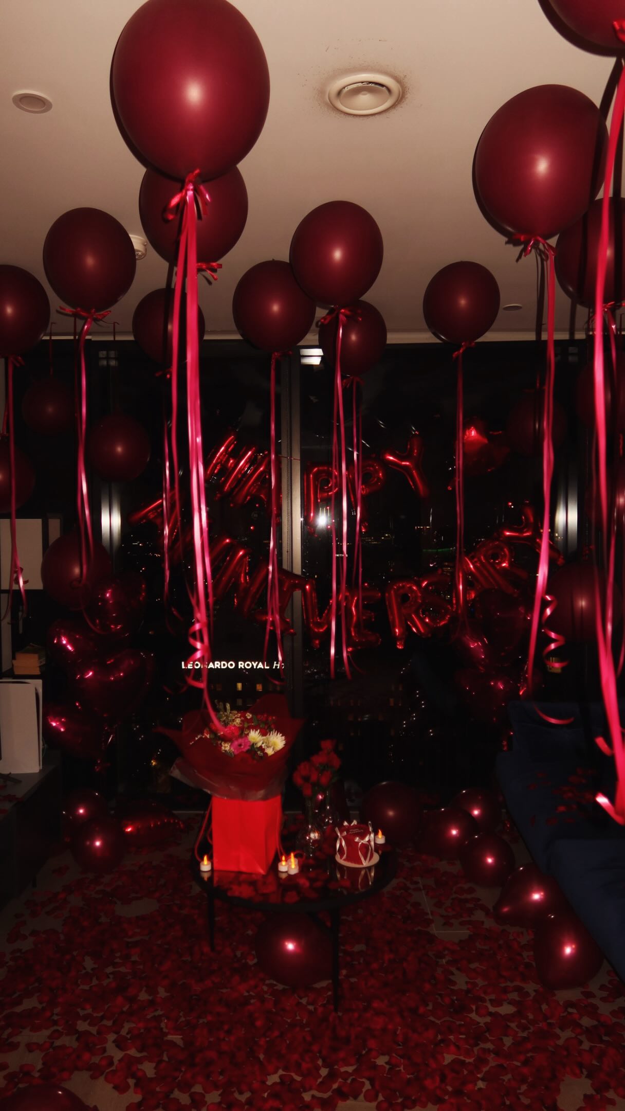 Romantic anniversary room with deep red balloons, roses and scattered petals